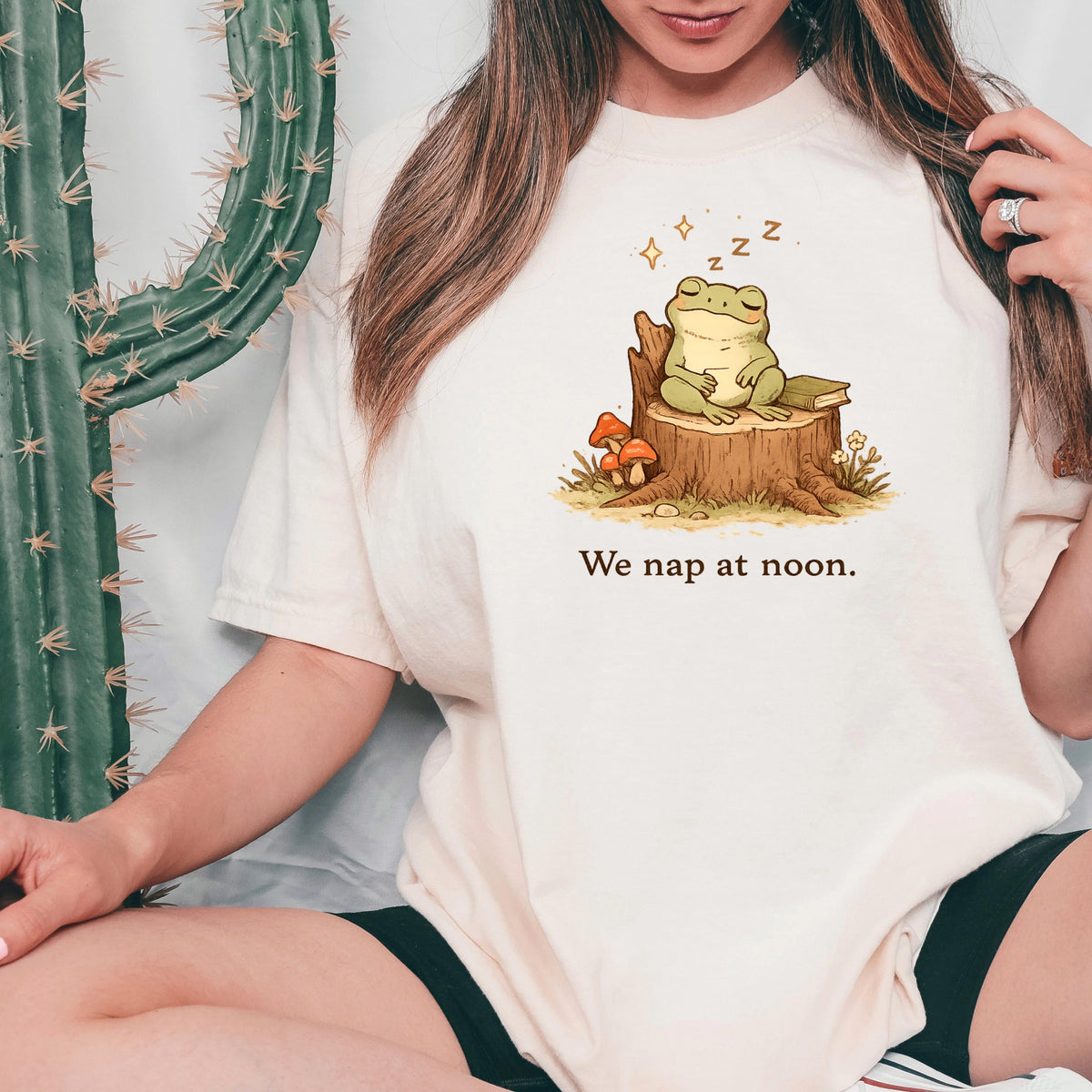 Ivory T-shirt with sleeping frog graphic and “We nap at noon.” text.