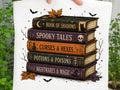 White graphic tee with stacked spooky books and bats, pumpkins, and leaf accents