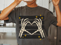 Dark graphic tee with white skeleton hands forming a heart and gold sparkle accents