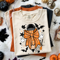 Cream graphic tee with jack-o'-lantern style character, bow, bats and stars