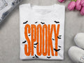 White graphic tee with orange SPOOKY lettering and black splatter accents
