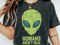 Dark gray graphic tee with green alien face and text “Humans Aren’t Real”