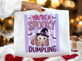 White graphic tee with purple 'You're a Spooky Dumpling' cauldron character