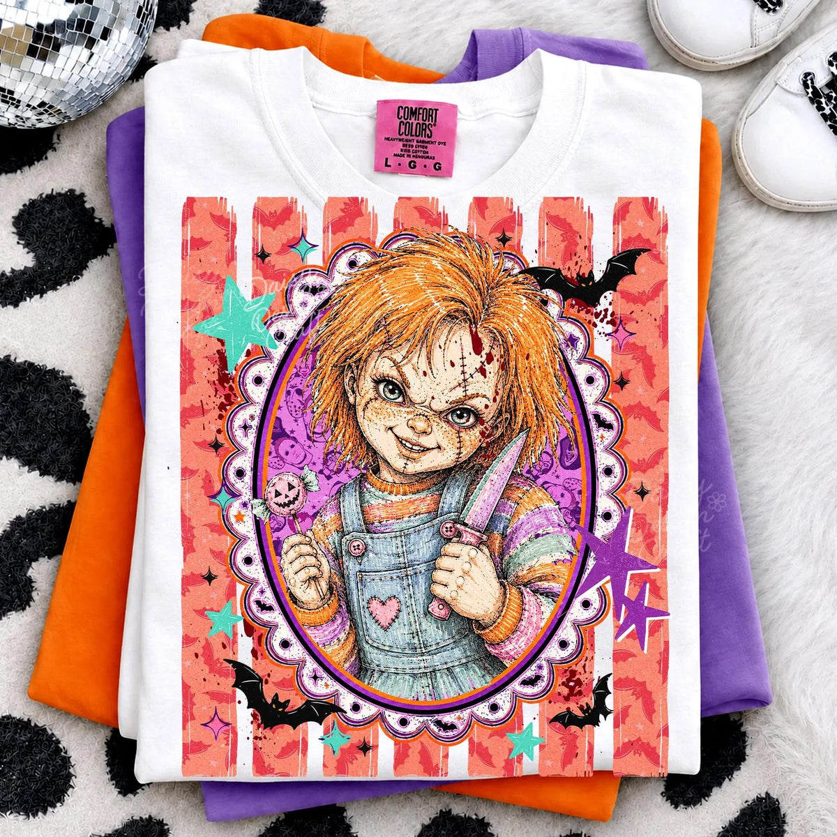 White graphic tee with colorful cartoon doll face in purple oval frame, heart details