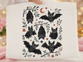 White graphic tee with black bat illustration and leafy floral accents