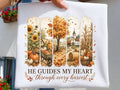 White harvest graphic tee with autumn scene and 'He Guides My Heart Through Every Harvest'