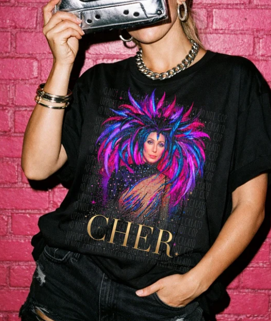 Black Cher graphic T-shirt with colorful portrait and gold “CHER” lettering on front