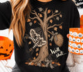 Black graphic tee with witch-themed tree, broom, and autumn leaves print