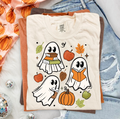 White short-sleeve graphic tee with reading ghosts, pumpkins, and autumn leaves print