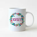 White ceramic mug with colorful floral wreath and the name "ASHLEY"