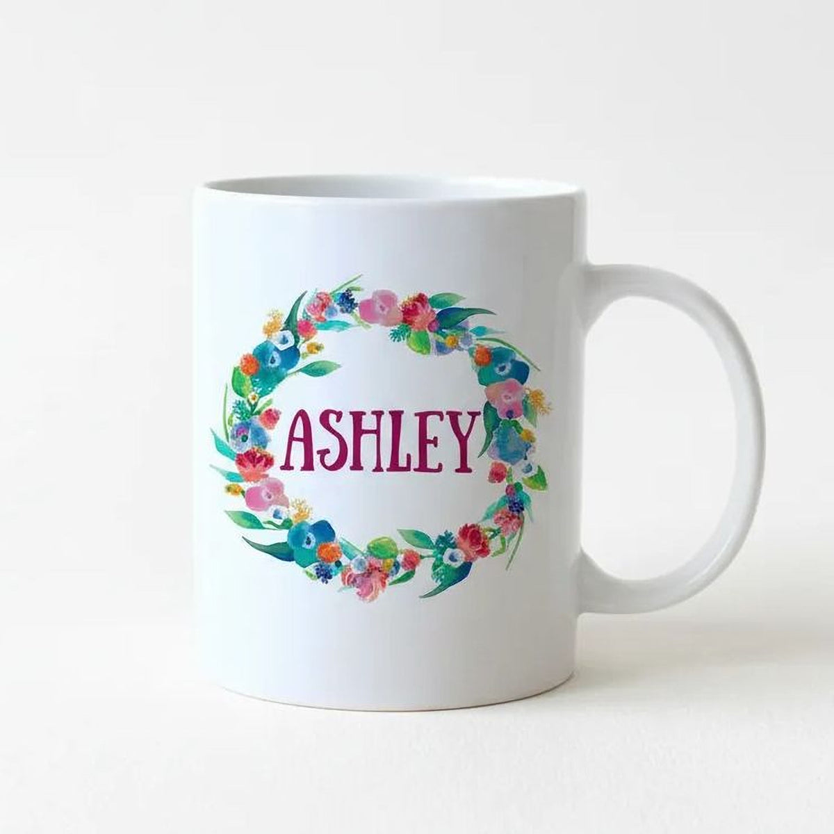White ceramic mug with colorful floral wreath and the name "ASHLEY"