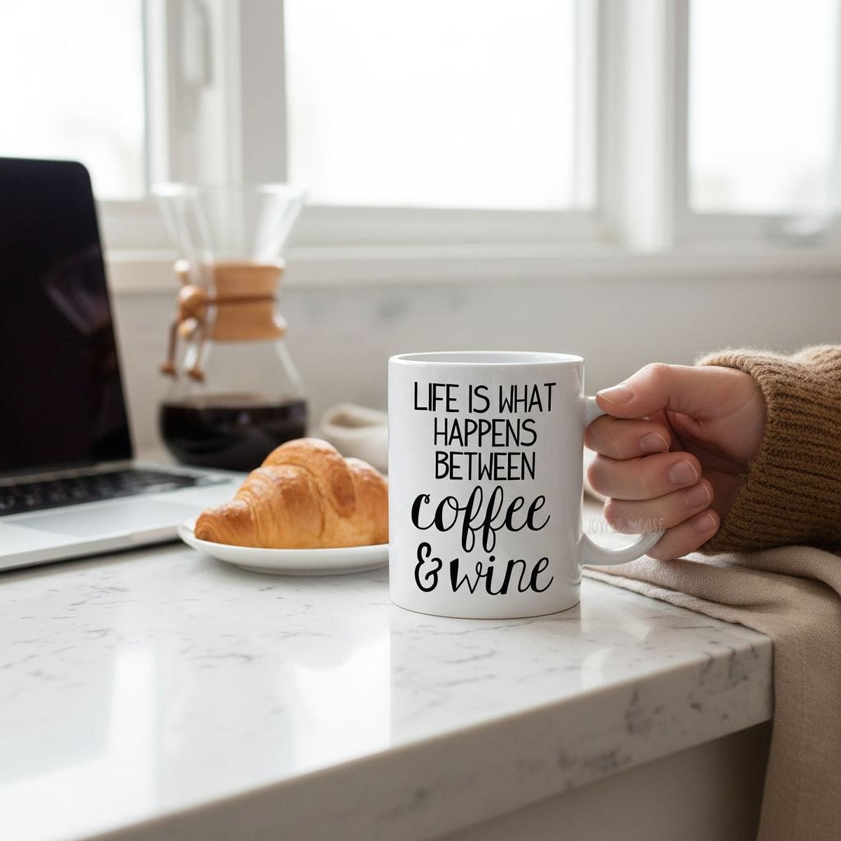White ceramic coffee mug in hand, printed “Life is what happens between coffee & wine”.