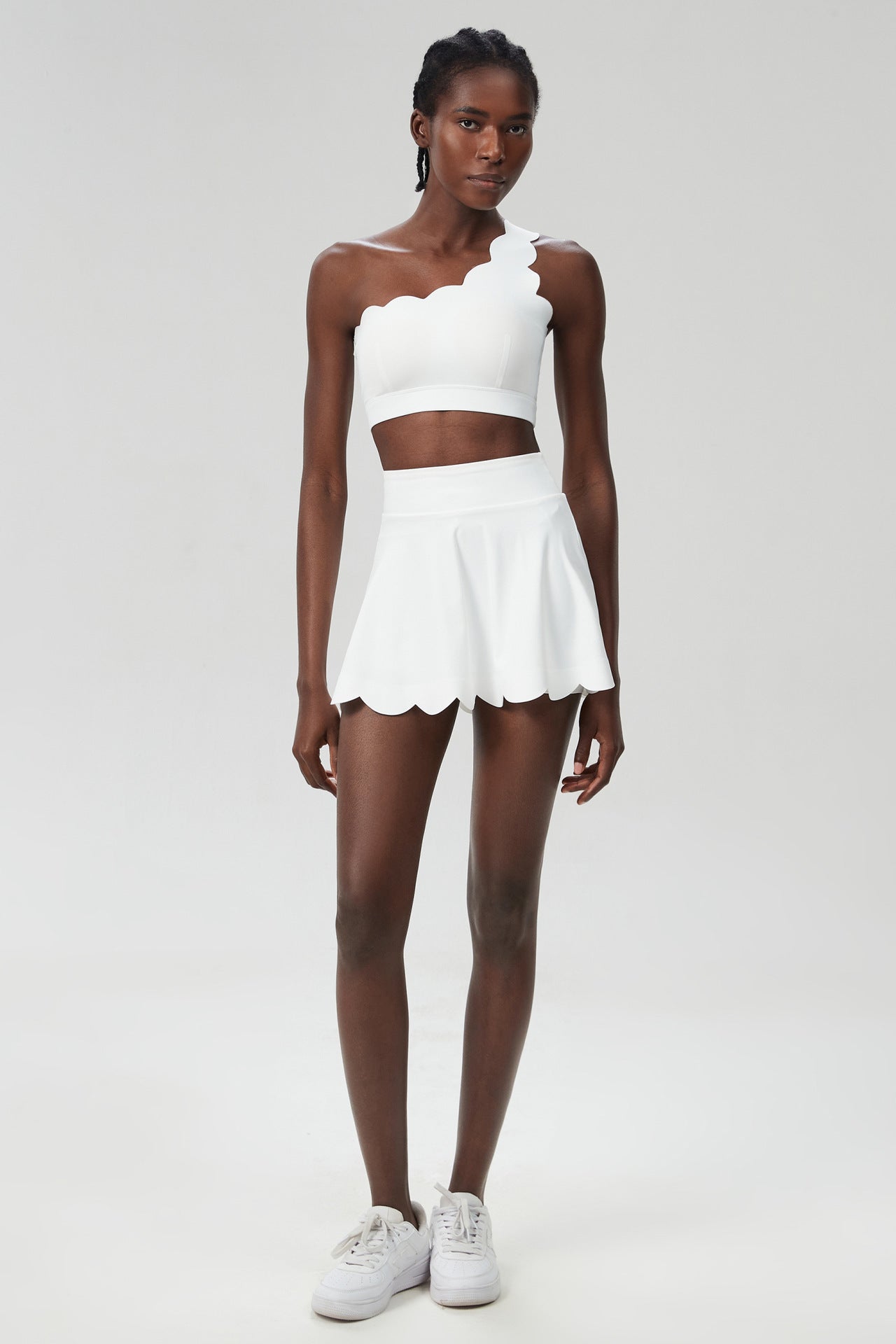 White one-shoulder sports two-piece set with cropped top and scalloped skater skirt.
