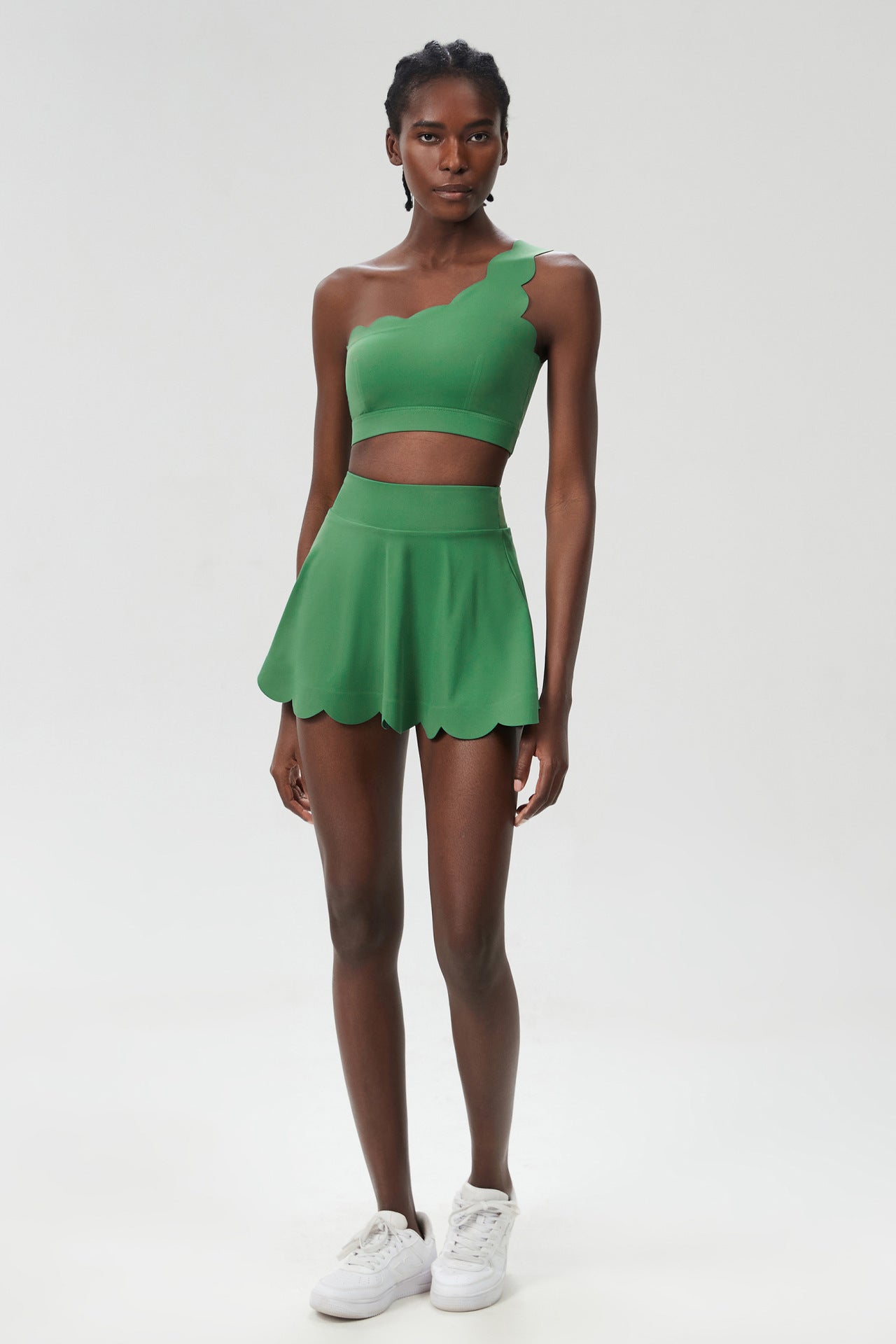 Green one-shoulder sports two-piece set with cropped top and scalloped skater skirt.