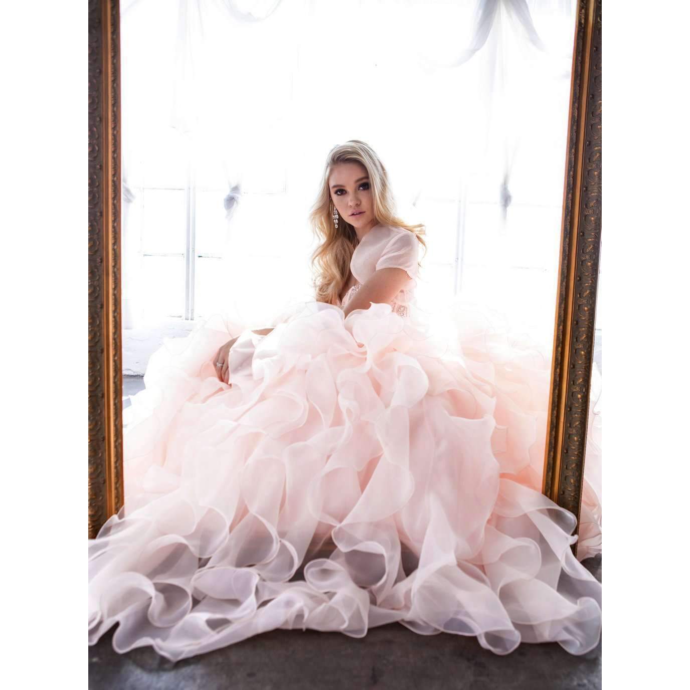 Light pink strapless ball gown with beaded corset bodice and layered organza ruffle skirt, seated