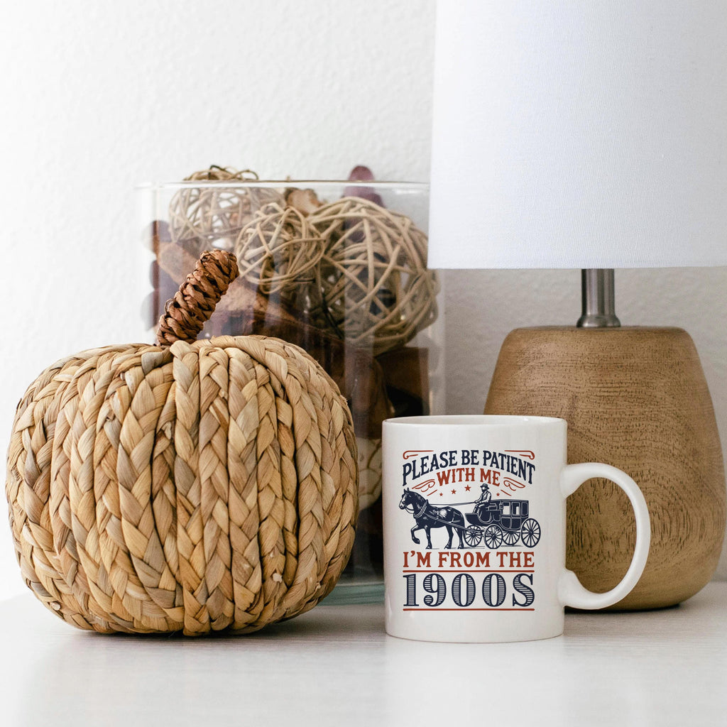 White ceramic mug on a tabletop with horse carriage graphic and “I’m from the 1900s”.