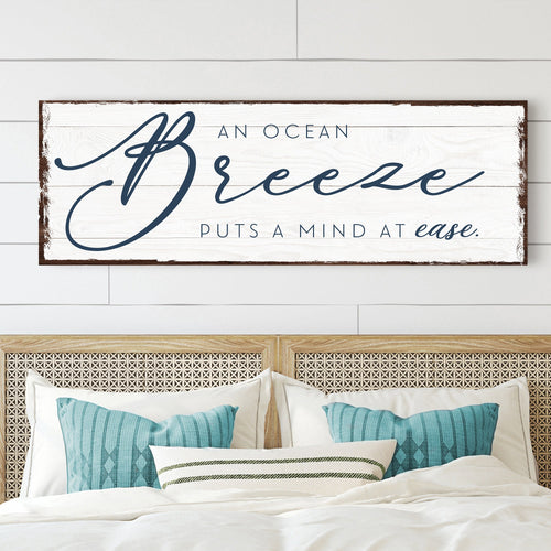 Ocean Breeze wall sign above bed, white canvas with blue script text and dark wood frame