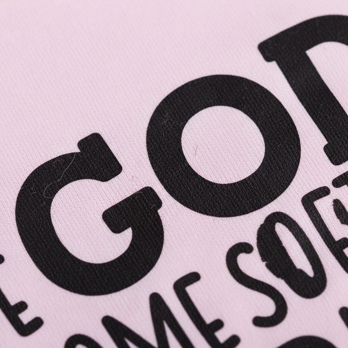 Light pink T-shirt close-up with bold black “GOD” and partial “CHILDREN” text print
