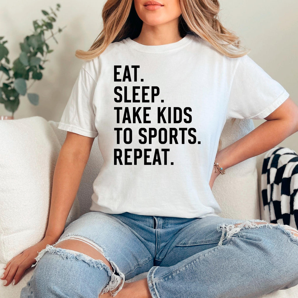 White unisex graphic tee with black text: EAT SLEEP TAKE KIDS TO SPORTS REPEAT.