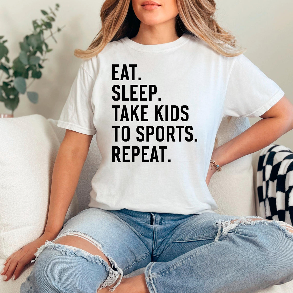 White unisex graphic tee with black text: EAT SLEEP TAKE KIDS TO SPORTS REPEAT.