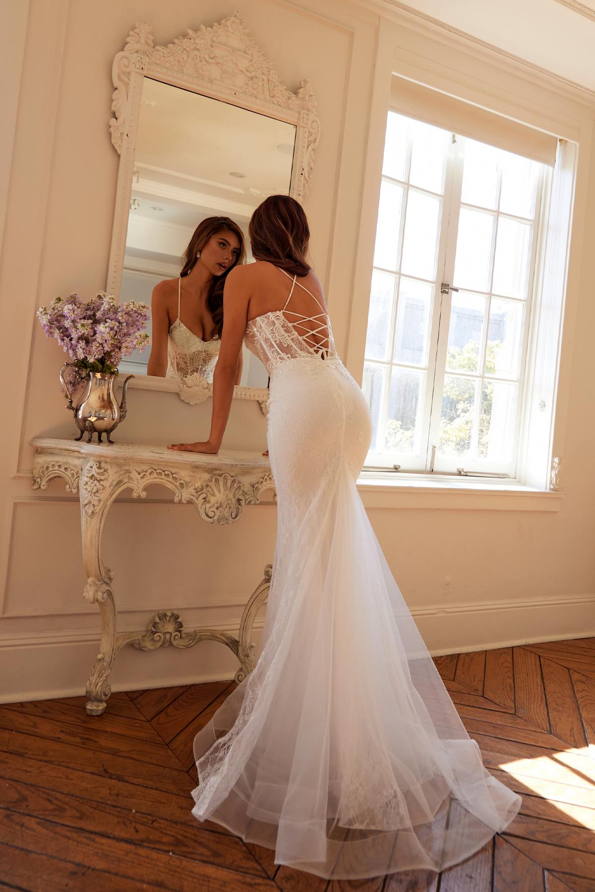 Off-white lace mermaid bridal dress with crisscross lace-back straps and flowing tulle hem.