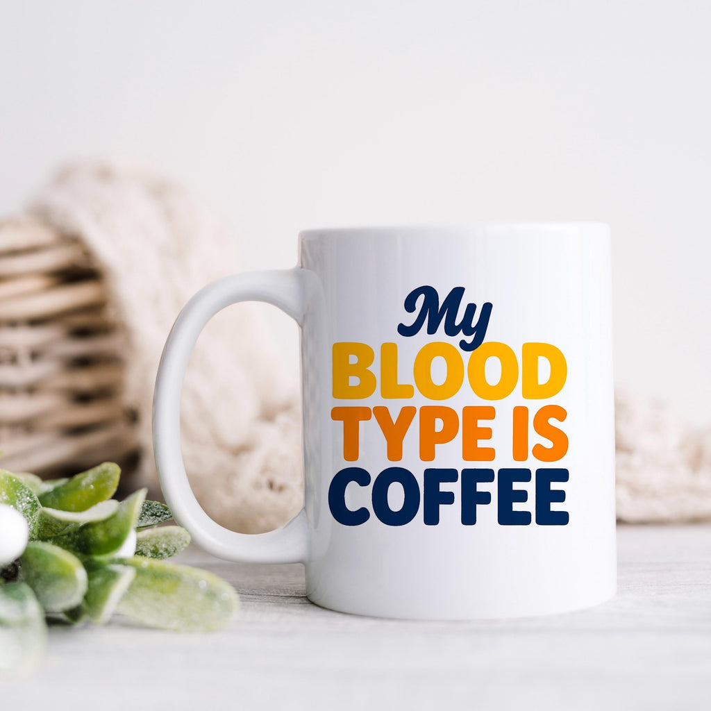 White ceramic coffee mug with handle, “My BLOOD TYPE IS COFFEE” printed on front.