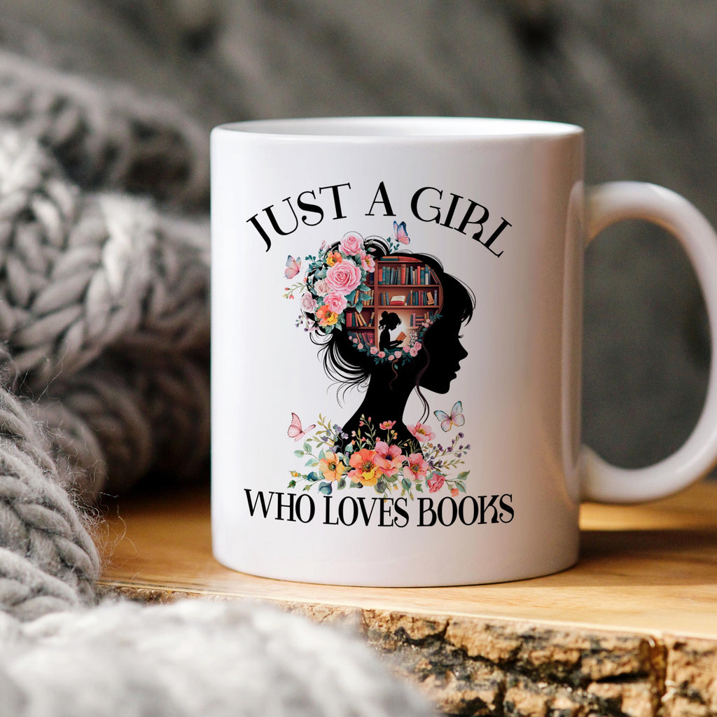 White ceramic coffee mug with “JUST A GIRL WHO LOVES BOOKS” graphic and floral book illustration.
