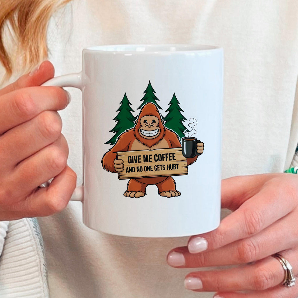 White ceramic coffee mug with Bigfoot graphic, held by hands.