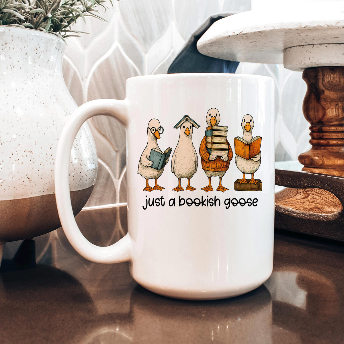 White ceramic mug featuring four bookish geese stacked books and "just a bookish goose"