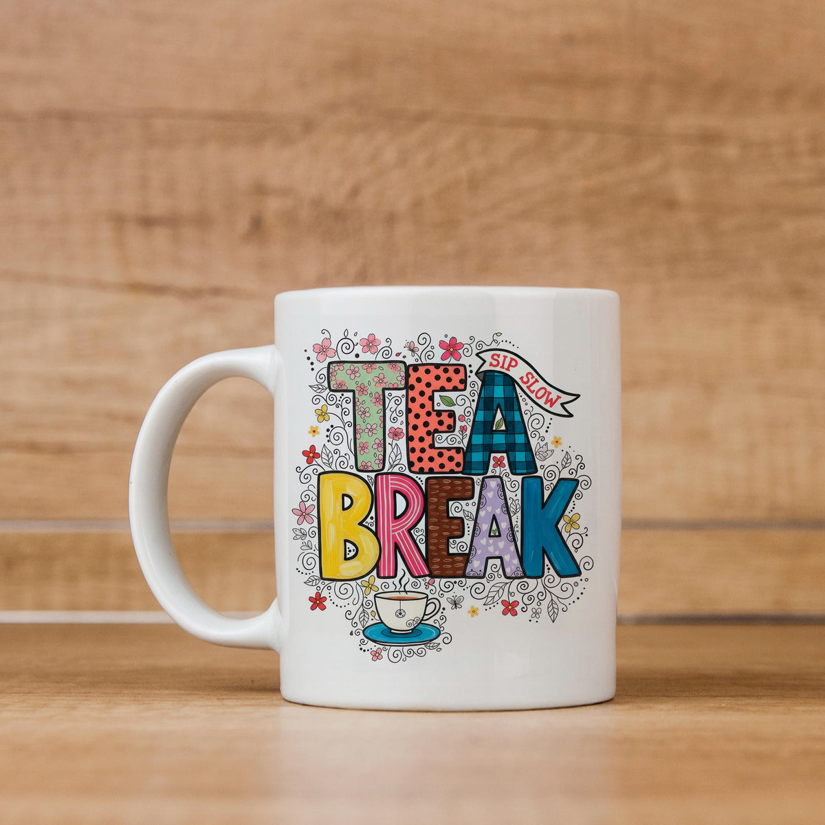 White ceramic tea mug with 'TEA BREAK' graphic, handle visible, colorful floral details