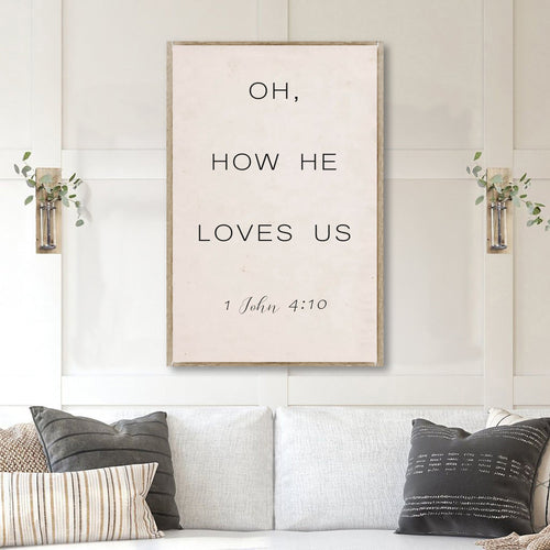 Canvas wall sign reading “OH, HOW HE LOVES US” with “1 John 4:10”