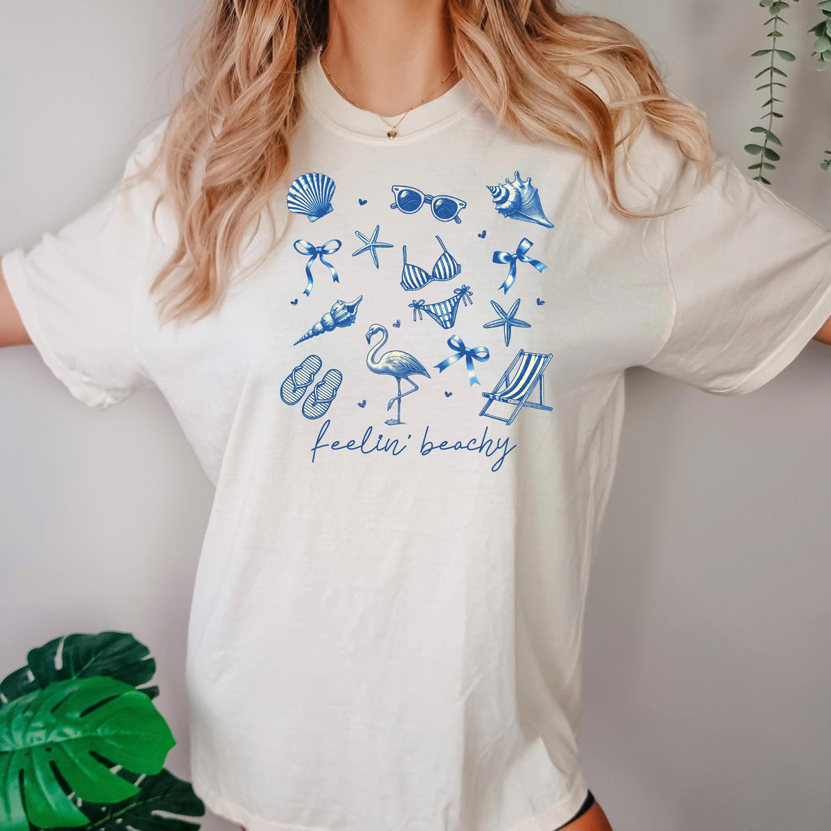White beach graphic unisex tee with blue shells, flamingos, and “feelin’ beachy” print