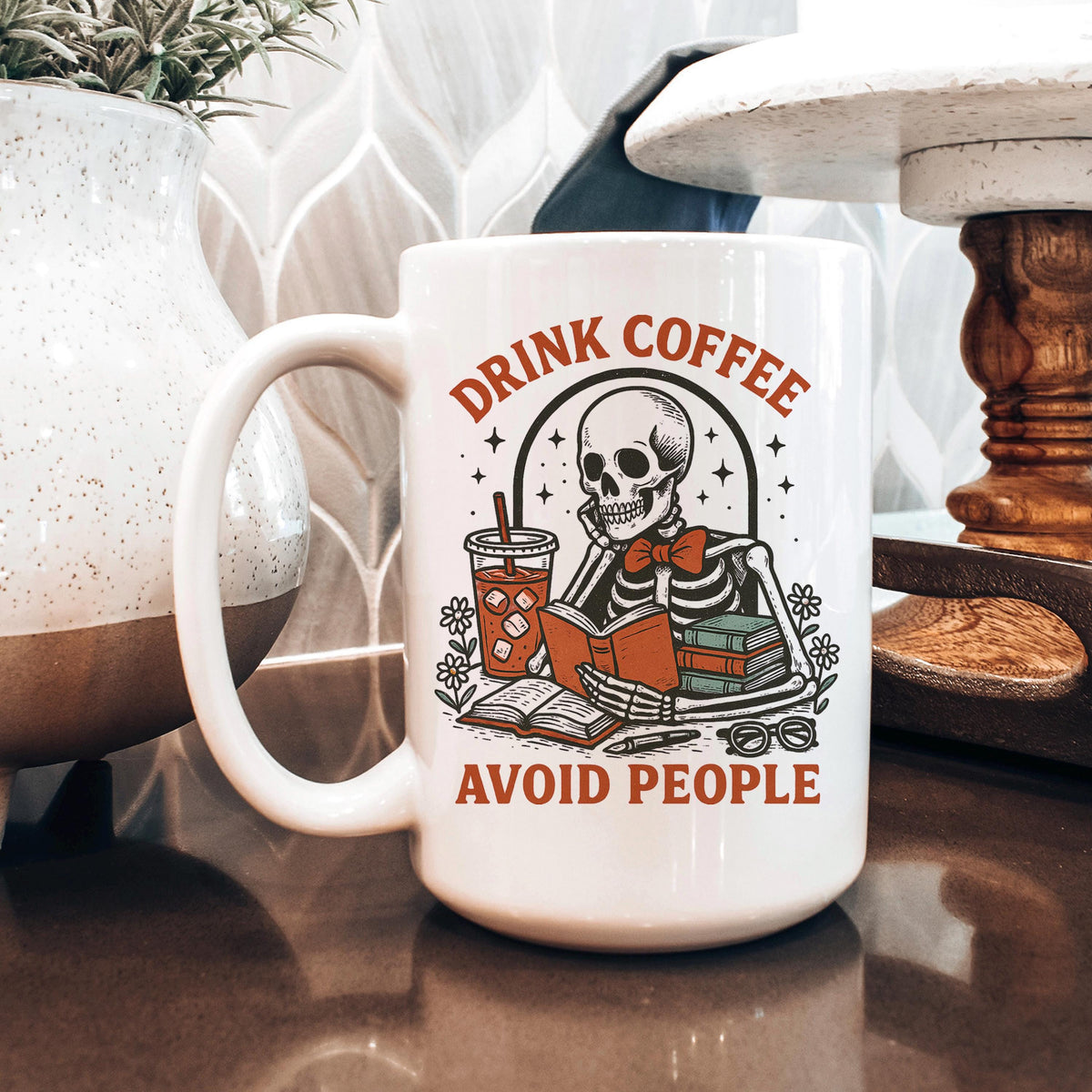 White coffee mug with skeleton design and red 'Drink coffee' and 'Avoid people' text