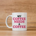 White ceramic coffee mug with "MY COFFEE NEEDS A COFFEE" pink and black text