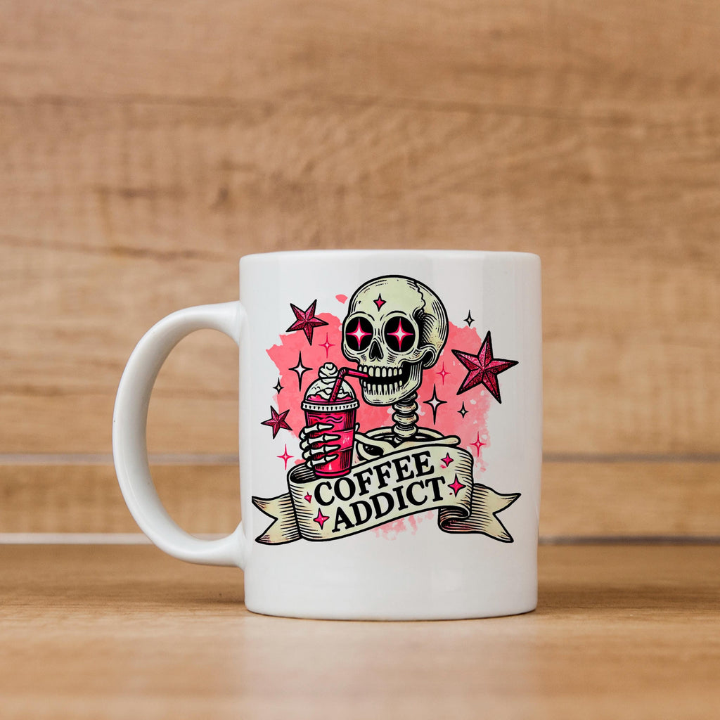 White ceramic coffee mug with pink skull and 'Coffee Addict' graphic, front view on tabletop
