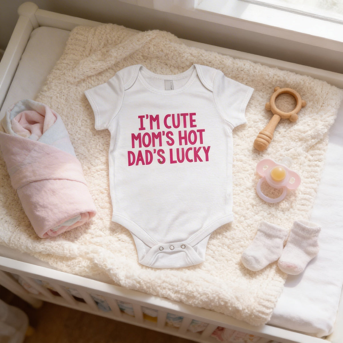 White newborn short-sleeve bodysuit with pink text slogan, laid on a soft blanket
