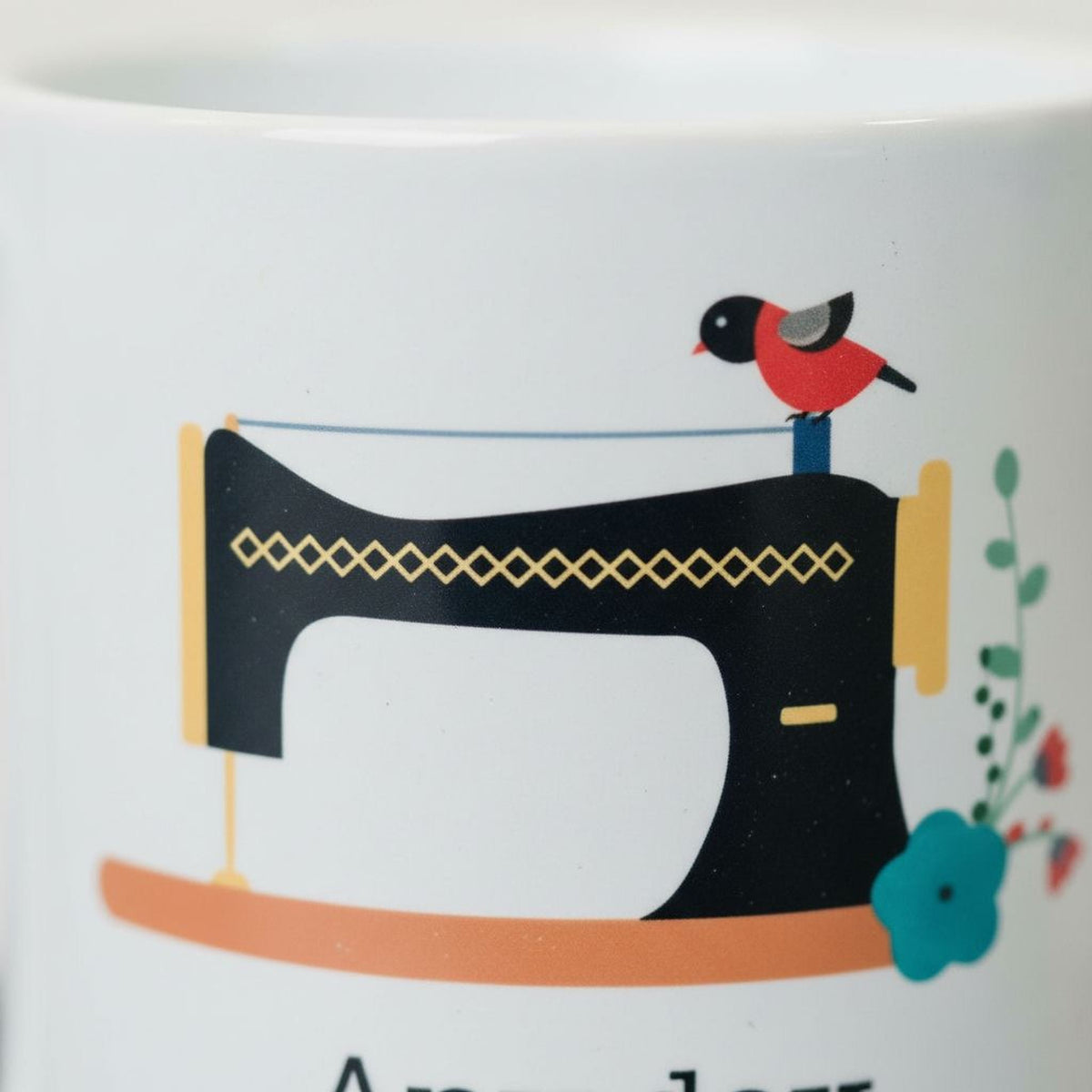 Close-up of white coffee mug showing black sewing machine illustration and red bird