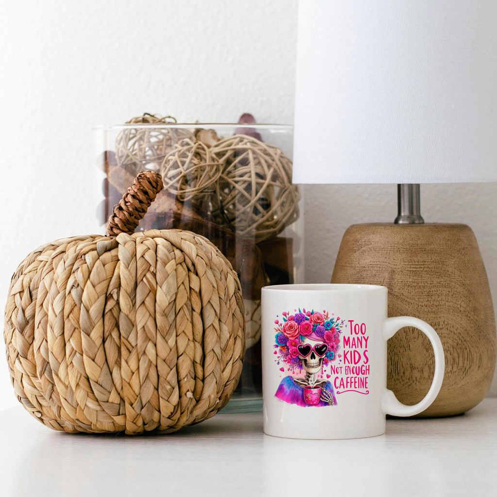 White ceramic mug with colorful floral crown skull graphic and pink “Too Many Kids” text.