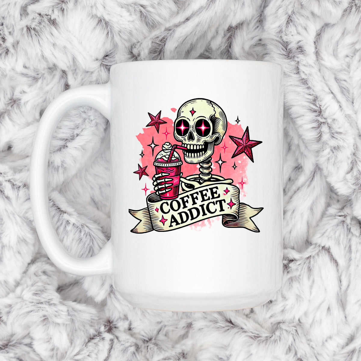 White ceramic coffee mug with pink skull and 'Coffee Addict' graphic, on fluffy gray fabric