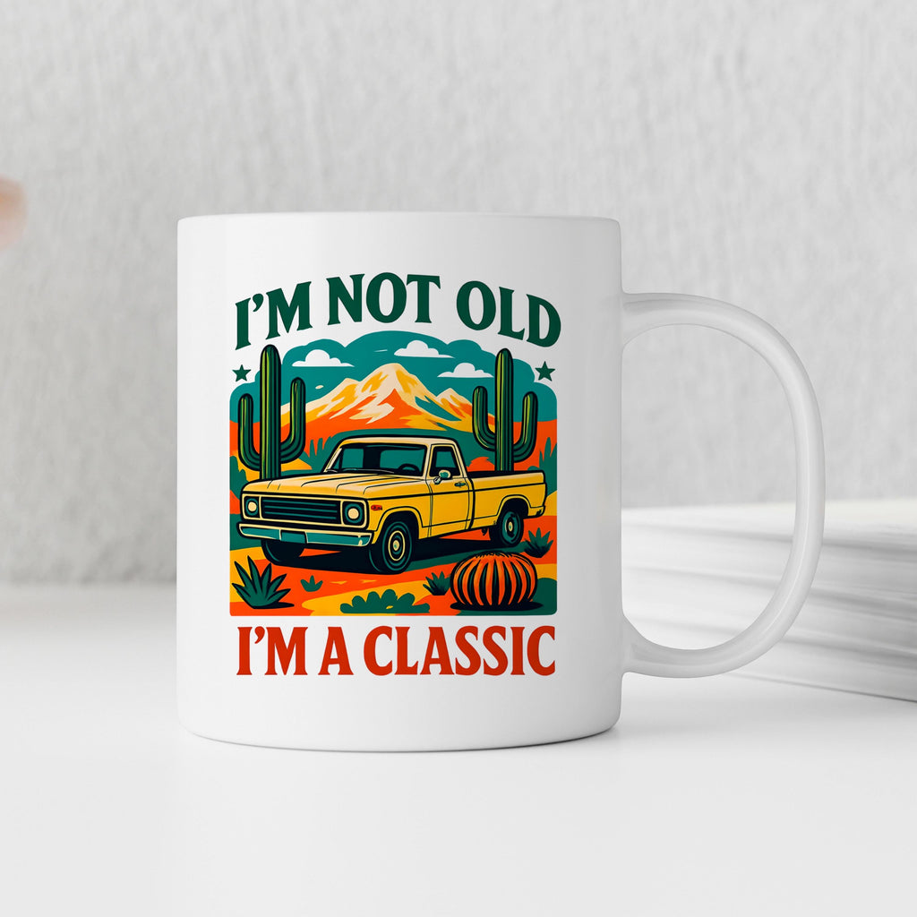 White ceramic mug with yellow vintage car and cacti graphic, text: “I’m not old, I’m a classic”.