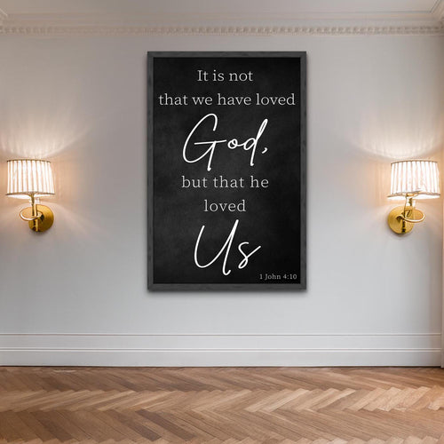 Black framed faith wall sign with white script quote 'God' and 'Us' (1 John 4:10)