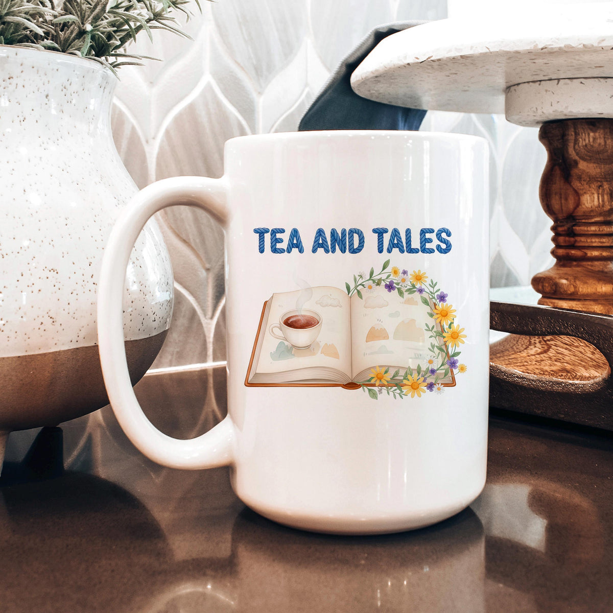 White ceramic mug with "TEA AND TALES" text and open book with flowers graphic