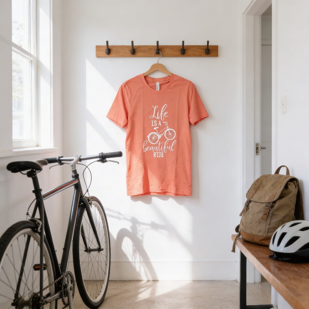 Coral graphic bicycle quote T-shirt on hanger with white “Life is a beautiful ride” design