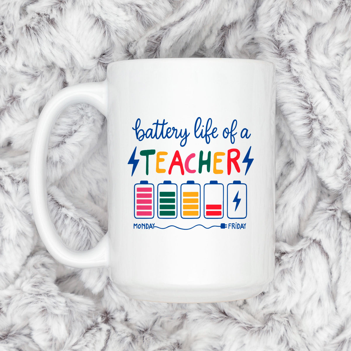 White ceramic mug with “battery life of a TEACHER” battery graphic on plush backdrop