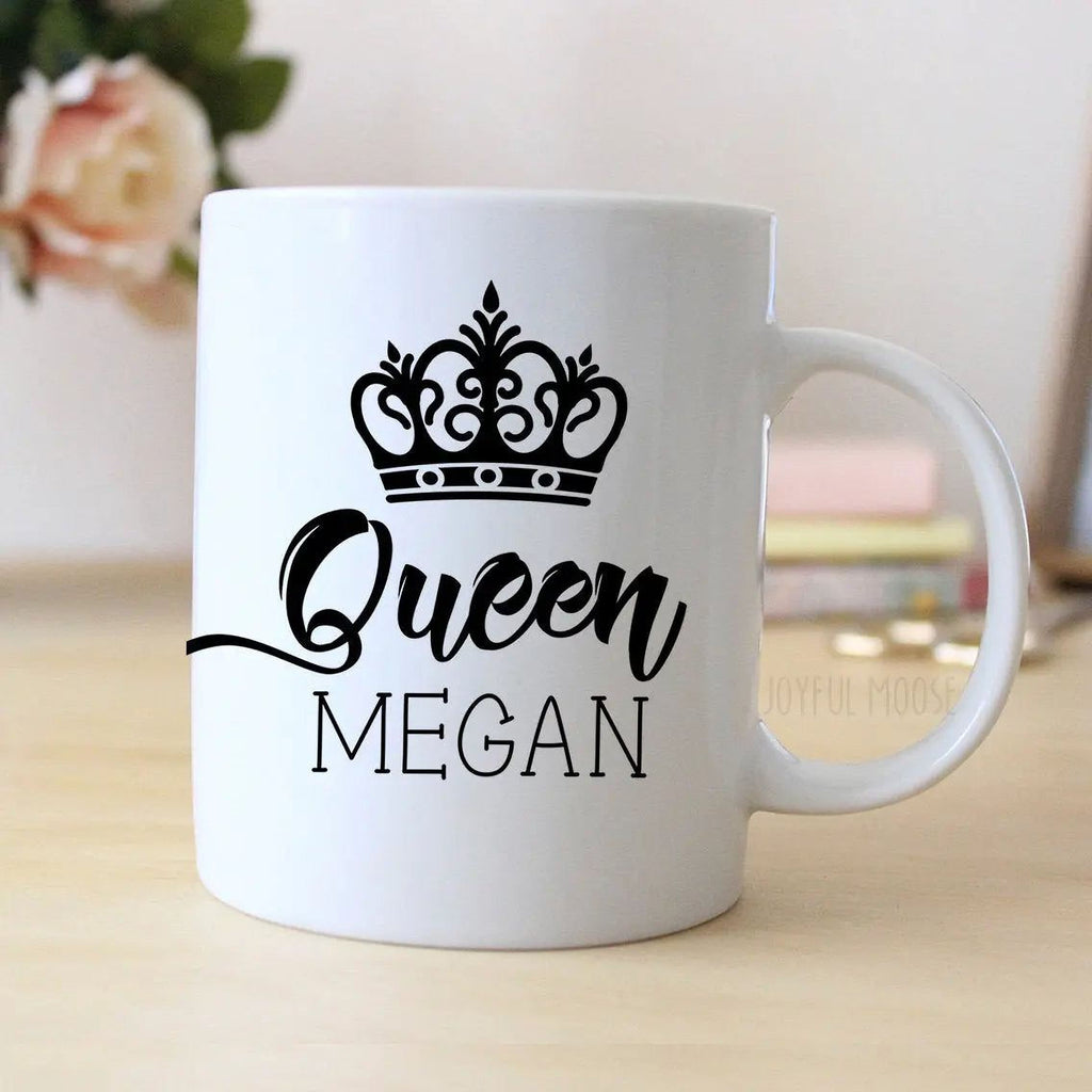 White ceramic mug with black crown and “Queen MEGAN” graphic, angled view with handle.