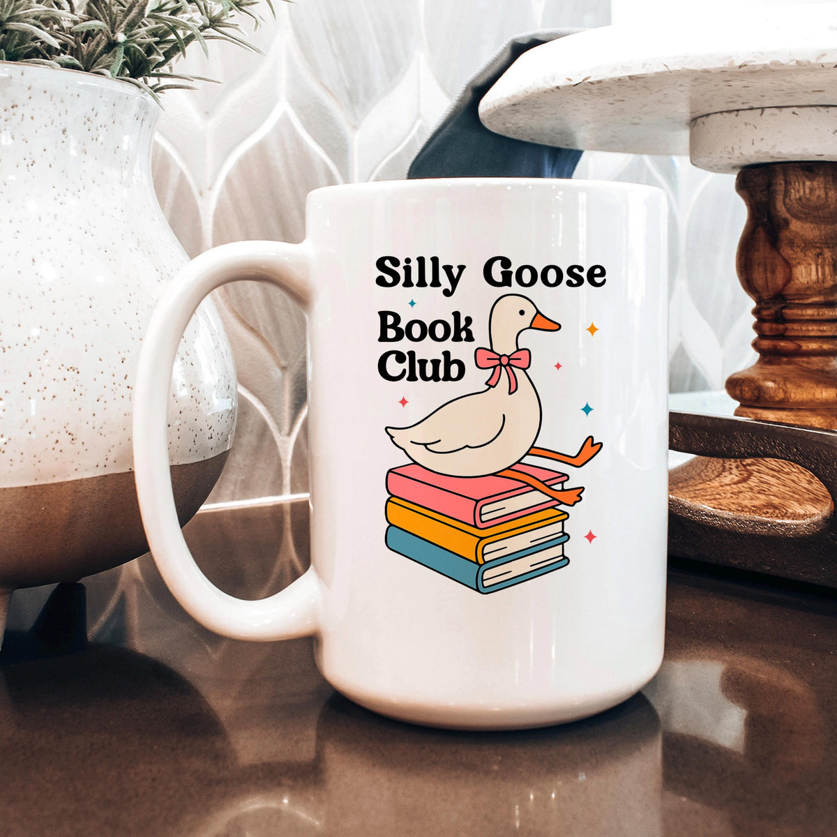 White ceramic coffee mug with goose-and-books illustration and 'Silly Goose Book Club' text.