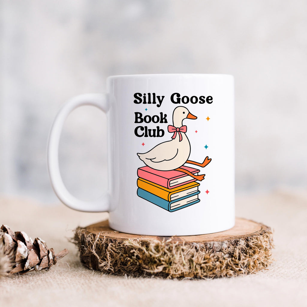 White ceramic mug on a coaster with cartoon goose and stacked books design.
