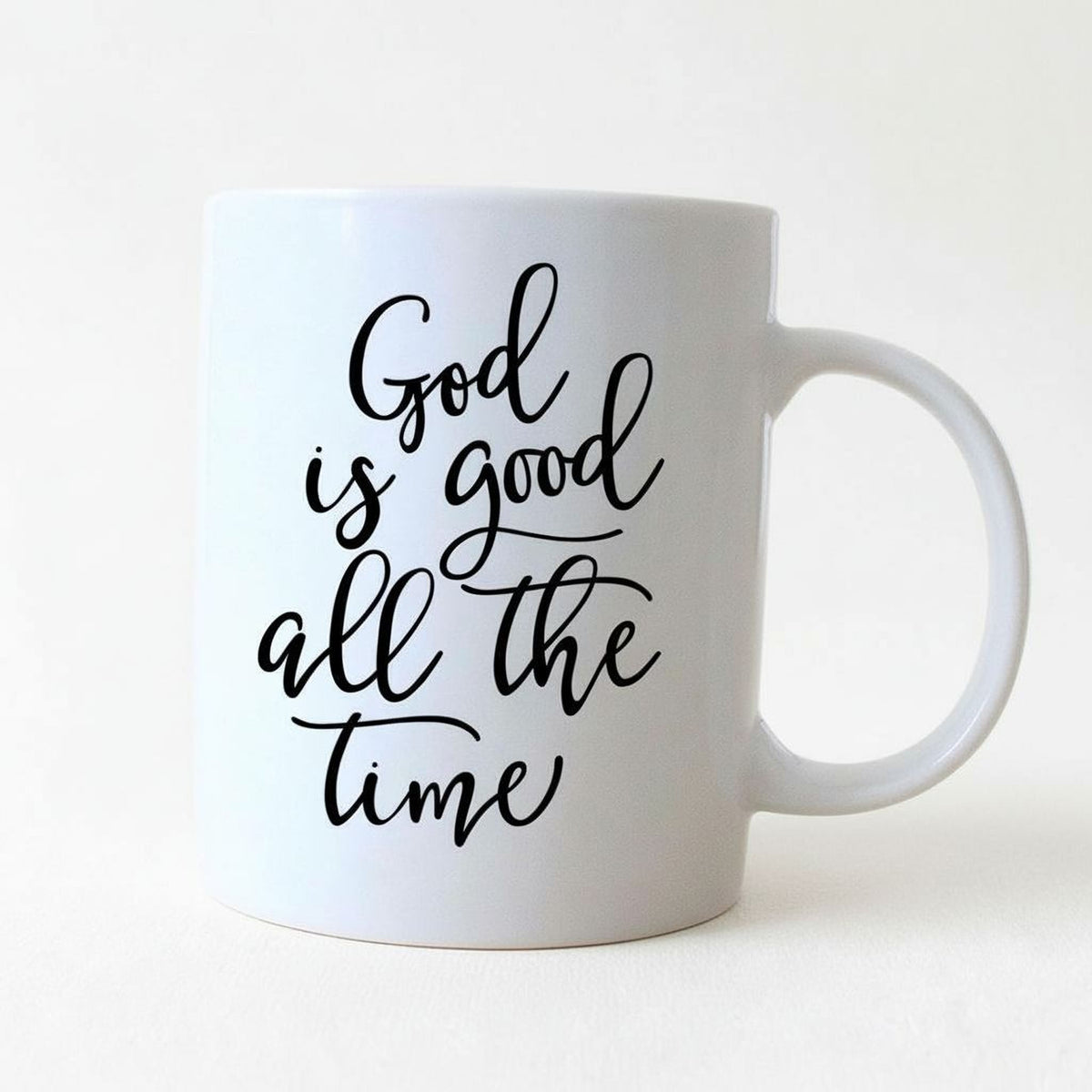 White ceramic coffee mug with 'God is good all the time' script on front