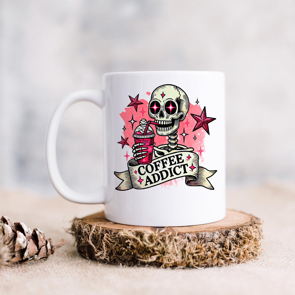 White ceramic coffee mug with pink skull 'Coffee Addict' graphic, standing on a round base