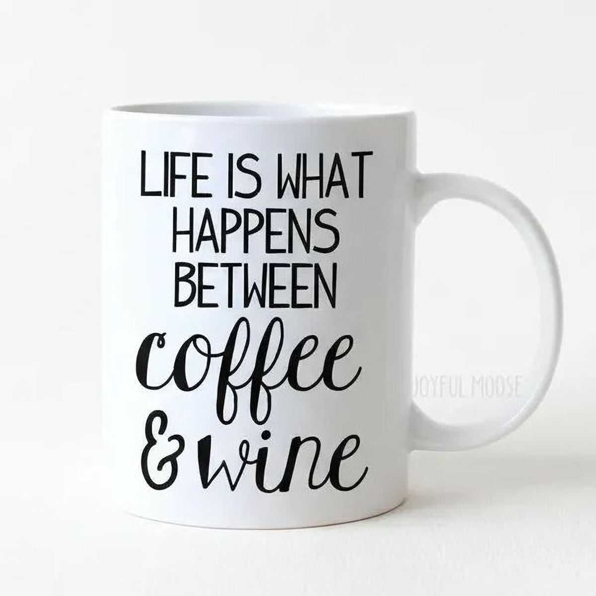 White ceramic coffee mug with black “Life is what happens between coffee & wine” text.